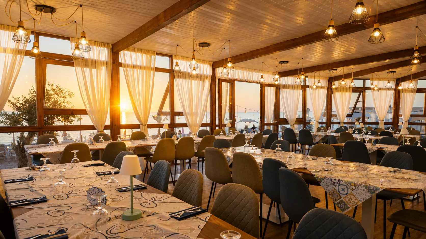 La sala interna del Golden Beach con i tavoli apparecchiati, vista mare al tramonto